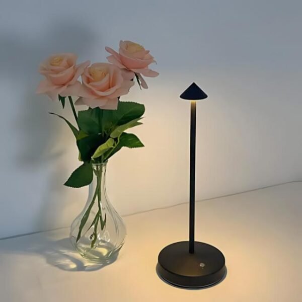 Minimalist black table lamp beside a vase with pink flowers.