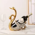Gold Couple Swan wine holder next to a glass of wine, adorned with silver.