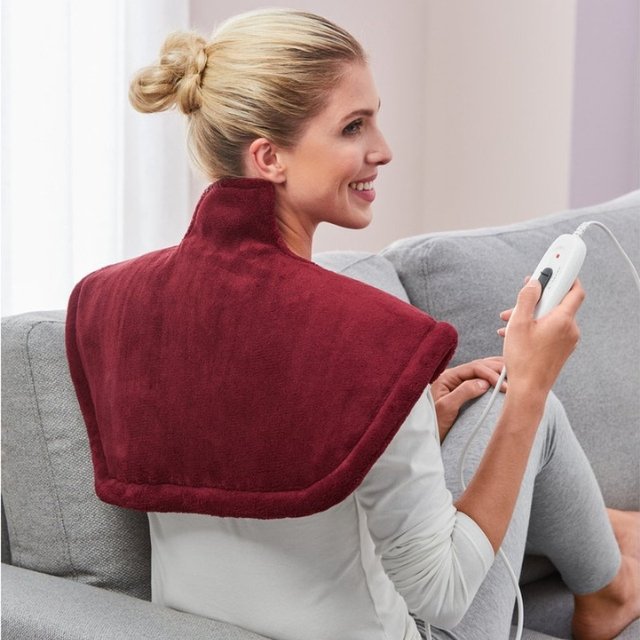 Woman using remote-controlled Sanitas massager with 6 heat levels.