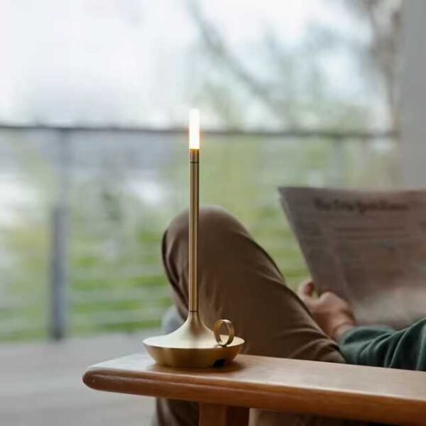 Aladdin table lamp in gold on armrest with man reading.