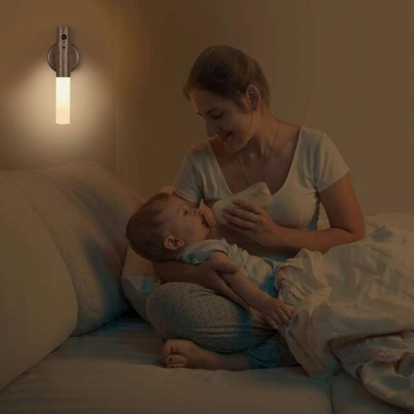 Mother feeding child under soft glow of motion sensor night light in dark room.