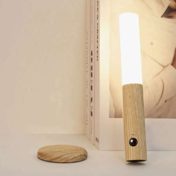 Motion sensor night light in light brown, emitting warm glow on bedside table.