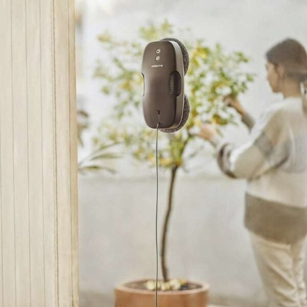 Woman taking care of plants while CREATE WipeBot window cleaning robot cleans windows.