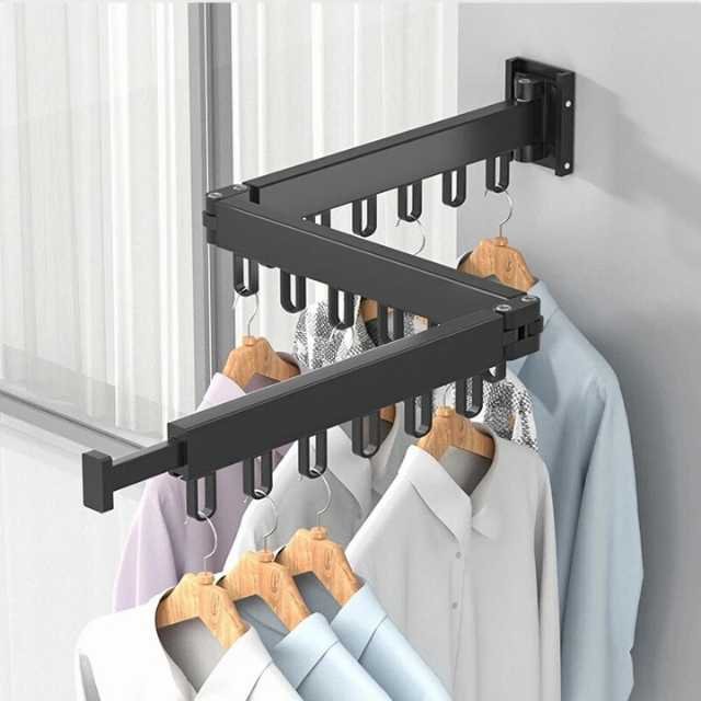 Foldable clothes drying rack in black mounted on wall holding shirts.