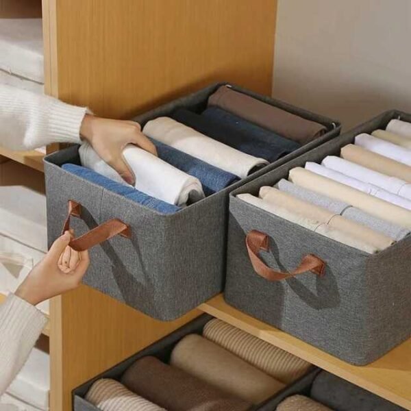 Woman using a foldable storage box to organize clothes on a shelf.