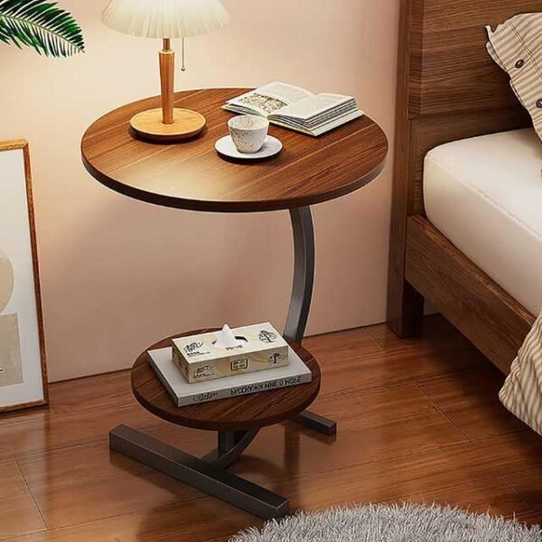 Round bedside table with two countertops, books, a cup of coffee, and a lamp.