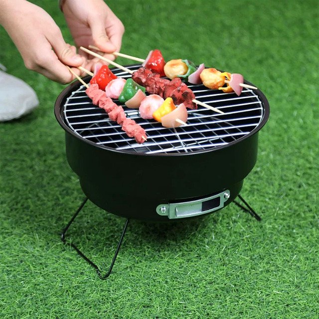 Man using portable outdoor grill to cook meat in a garden setting.