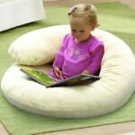 Baby sitting inside C-shaped pillow while reading a book.