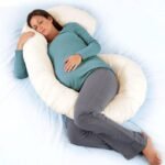 Pregnant mom sleeping with C-shaped maternity pillow for belly support.