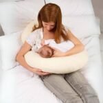 Mom using C-shaped pregnancy pillow for breastfeeding support.