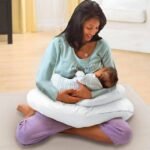 Mom holding baby while using C-shaped pillow for comfort and support.