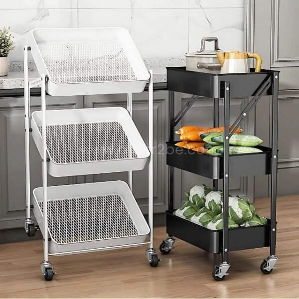Two storage carts in a kitchen, one black with solid trays holding vegetables and one white with mesh trays, both on wheels for mobility.