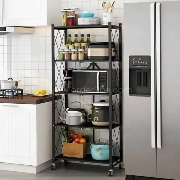 Black metal 5-tier shelving unit between a counter and refrigerator, storing kitchen items like plates, jars, and a microwave.