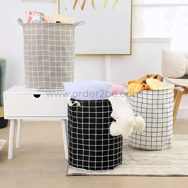 Set of three cylindrical laundry bags with grid pattern in grey, black, and white, featuring carry handles in a cozy room setting.