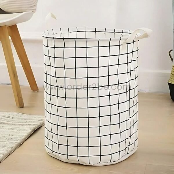 White laundry basket with black grid pattern and carry handles, placed on a wooden floor.