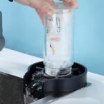 A hand cleaning a glass bottle with the automatic cup and glass washer’s high-pressure jets.