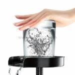 A hand using the automatic cup and glass washer to clean a drinking glass with high-pressure jets.