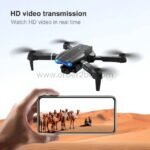 E99 Pro Foldable Drone flying above a hand holding a smartphone, displaying a live HD video feed of a desert landscape.