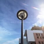 Circular LED streetlight against a blue sky, showcasing a sleek design with an industrial building backdrop, emphasizing durability and efficiency.