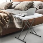 Folding coffee table placed by a bed, set up as a study station with a laptop and book.