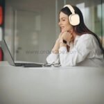 Woman wearing beige Green Lion Echo ANC Wireless Headphones while working at a desk, highlighting comfort and focus for work or leisure.