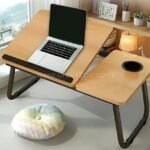 Black-legged wooden desk with a tilted laptop area and flat cup holder section on a light floor.