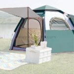 Automatic pop-up camping tent near a tranquil lake, accompanied by a cozy picnic setup on a colorful blanket.