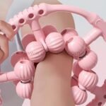 Close-up view of the pink handheld massager showing its detailed design and multiple rollers.