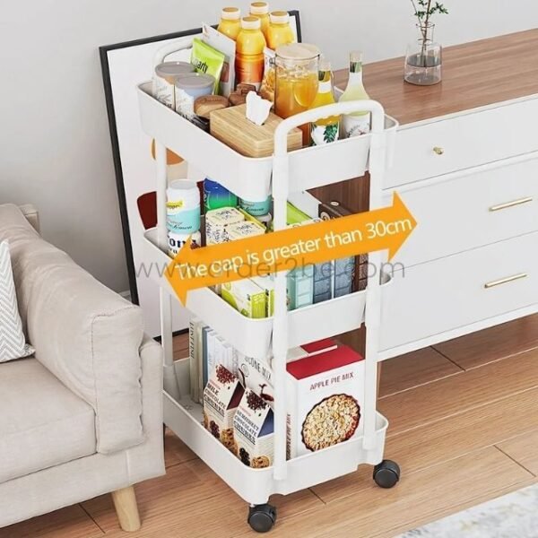 White 3-tier rolling organizer loaded with groceries, snacks, and books next to a dresser in a small kitchen.
