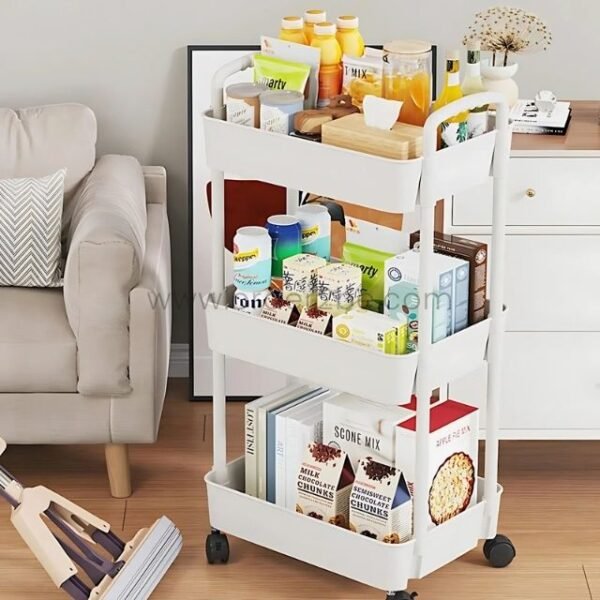White 3-tier rolling organizer holding books, snacks, and household items near a sofa in a living room.