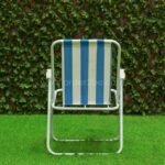 A classic striped beach chair with bold blue and white stripes is placed on artificial grass, framed by a lush green hedge.