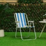 A classic striped beach chair with bold blue and white stripes sits gracefully on lush green grass, surrounded by a hedge and potted plant.