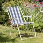 A classic striped beach chair with bold blue and white stripes is nestled among blooming flowers in a vibrant garden.