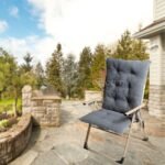 A comfortable camping recliner chair placed on a stone pathway near a garden, emphasizing its role in outdoor relaxation.