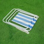 A classic striped beach chair with bold blue and white stripes is neatly folded flat on a grassy surface, showcasing its compact design.