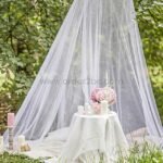 White bed mosquito net repurposed as an outdoor canopy over a candlelit table setting.