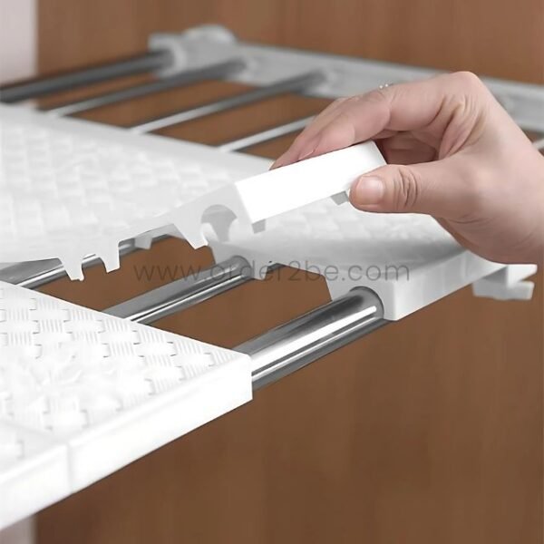 A hand adjusting the plastic top of the Adjustable Shelf Organizer to expand it across chrome rods.