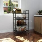 Portable multi-shelf storage rack holding plates, bowls, and snacks, set in a modern kitchen near a window.