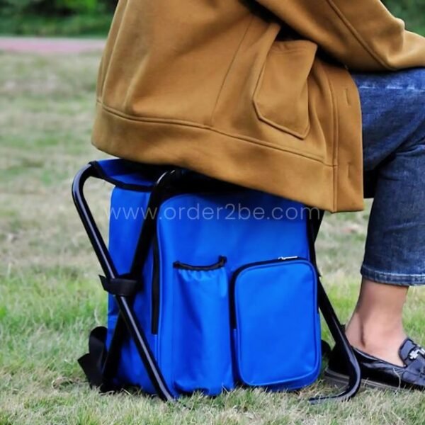 A person seated on a blue portable backpack chair in a grassy field.