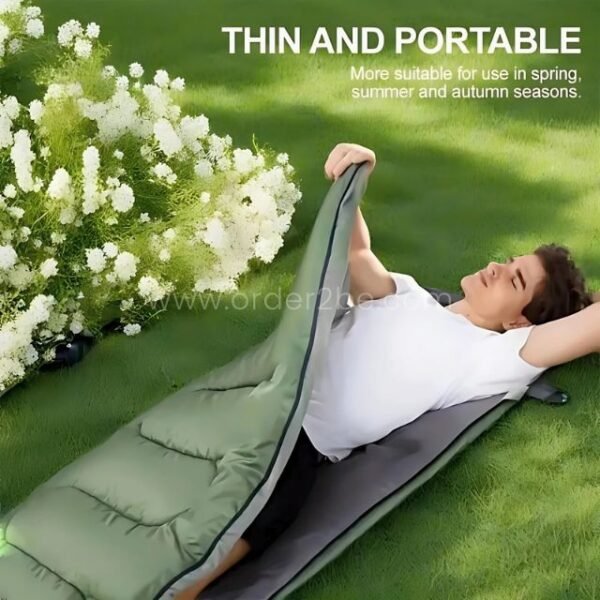 A man lounging in a thin green portable sleeping bag, perfect for spring, summer, and fall use, on grassy ground.
