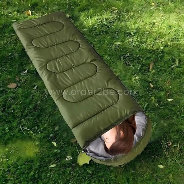 A green portable sleeping bag with gray interior stretched on grass, partially occupied, showcasing its outdoor usability.