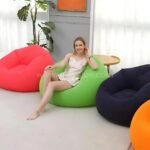 Woman sitting on a green inflatable bean bag chair among red, navy, and orange options, lightweight and portable.
