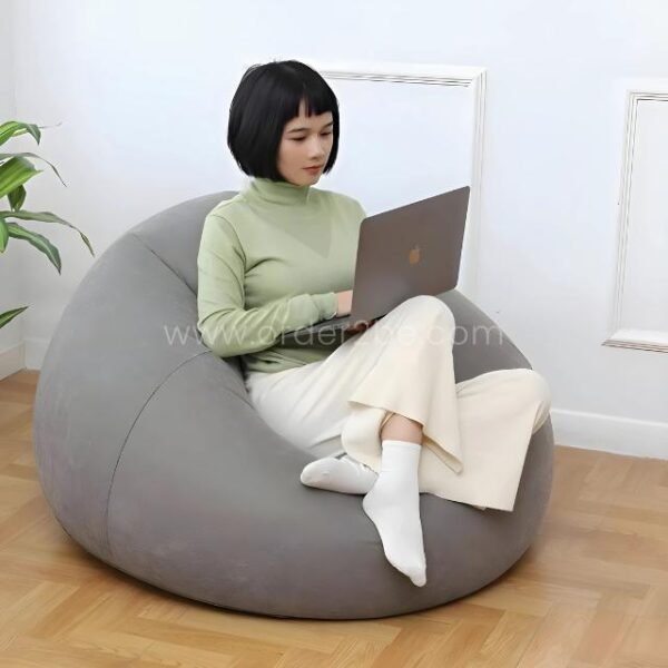 Woman working on a laptop while sitting on a gray inflatable bean bag chair for indoor use.