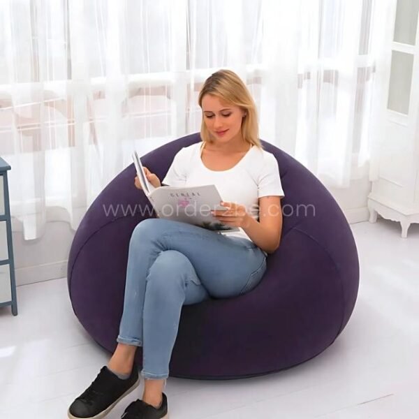 Woman reading a book on a navy inflatable bean bag chair, soft and supportive seating in a bright minimalist room.