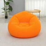 Orange inflatable bean bag chair in a bright room with coffee table, portable and easy to inflate.