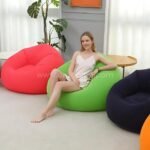 Woman seated on a green inflatable bean bag chair surrounded by other colorful options, lightweight and portable.
