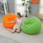 Woman sitting on the floor between orange and green inflatable bean bag chairs in a minimalist living room, easy to inflate and move.